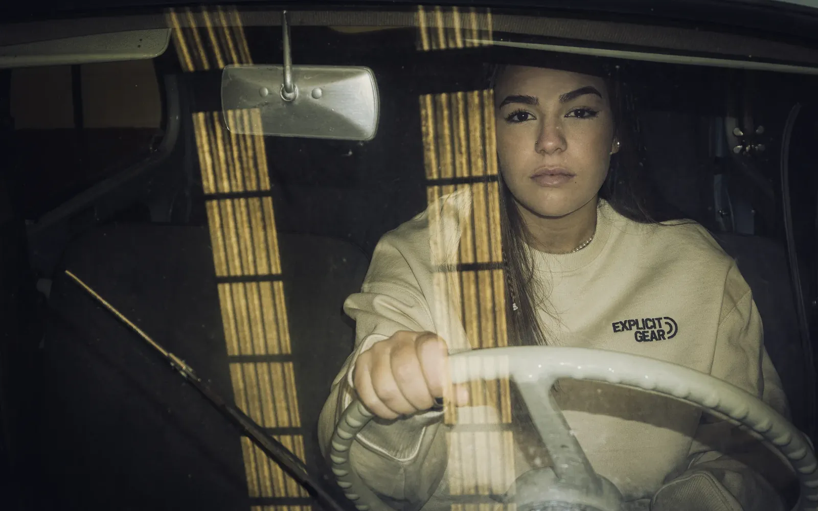 Chica con la sudadera crema de Explicit Gear al volante de un coche antiguo