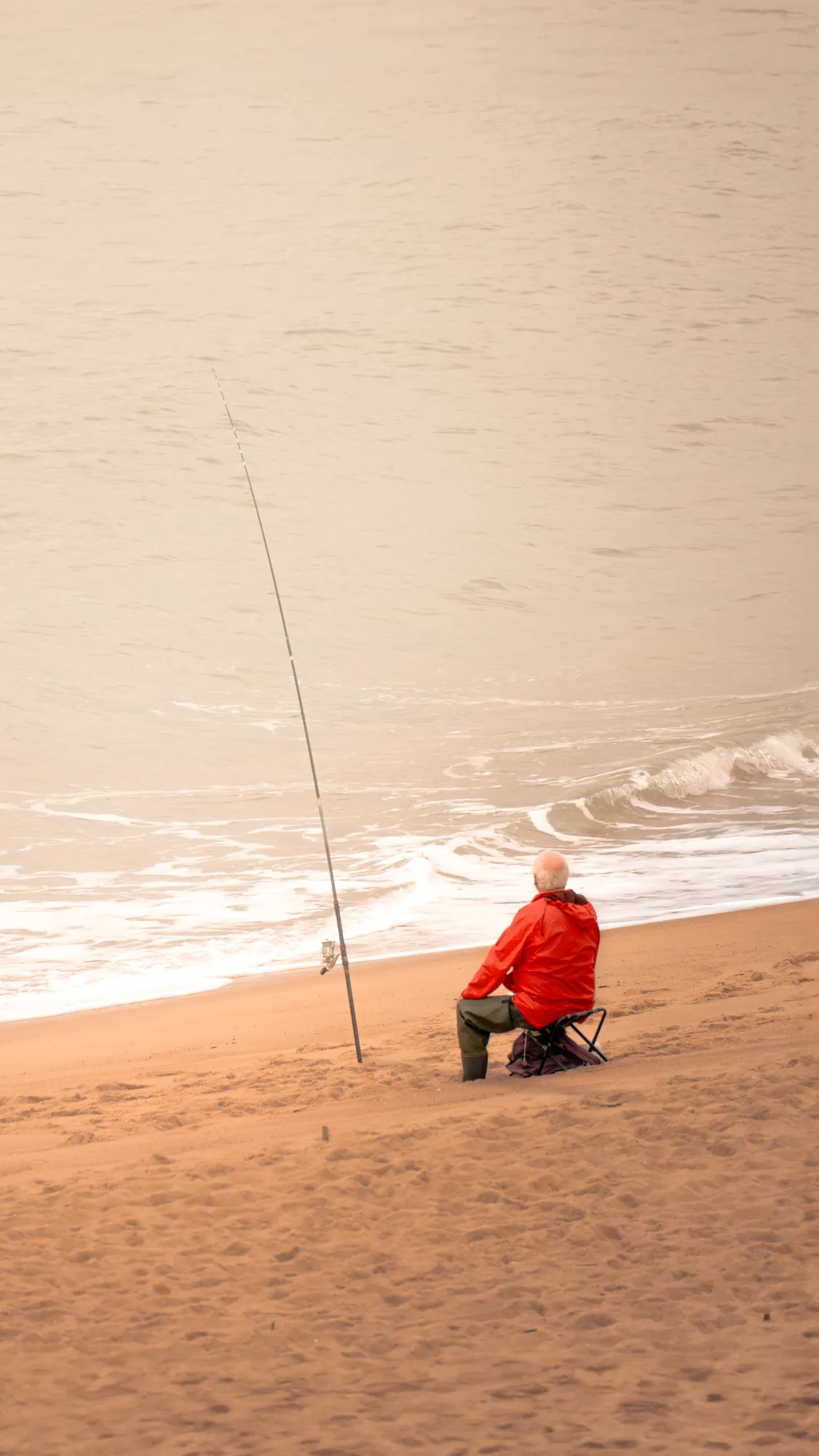 Pescador con chaqueta roja sentado en la arena