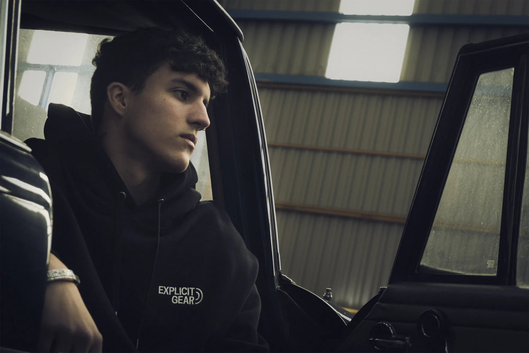 Chico con la sudadera negra de Explicit Gear dentro de un coche antiguo