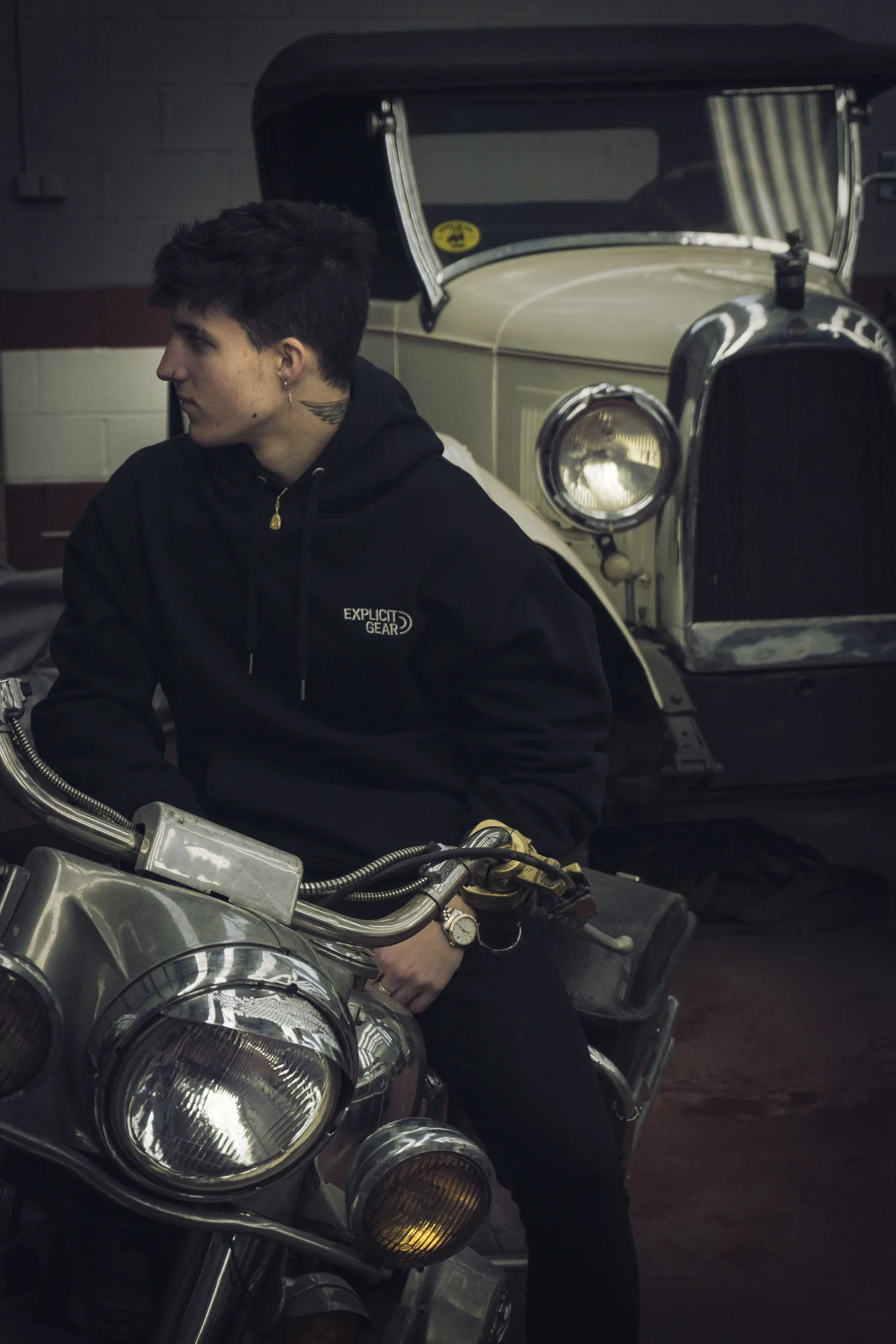 Chico con la sudadera negra de Explicit Gear sentado en una moto antigua