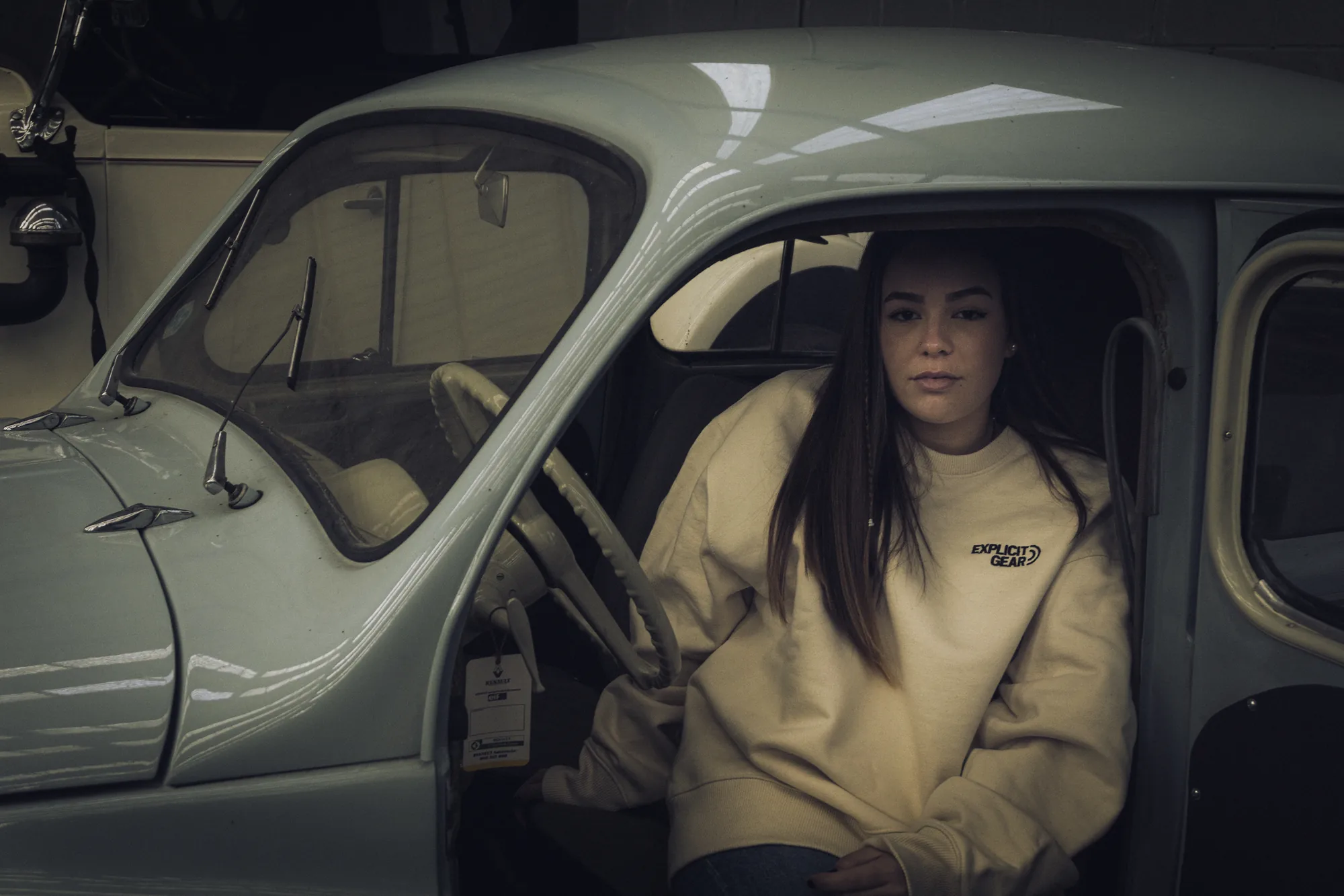 Chica con la sudadera crema de Explicit Gear en un coche clásico gris