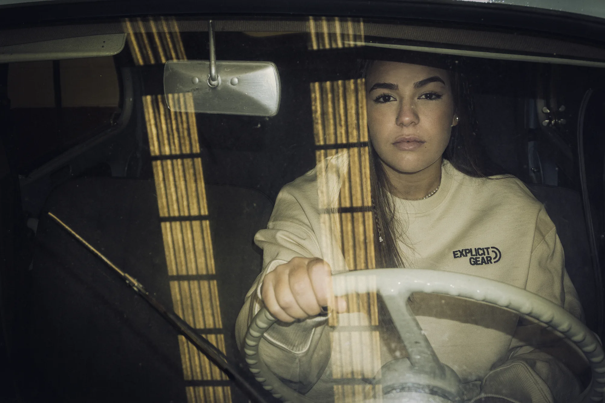 Chica con la sudadera crema de Explicit Gear al volante de un coche antiguo