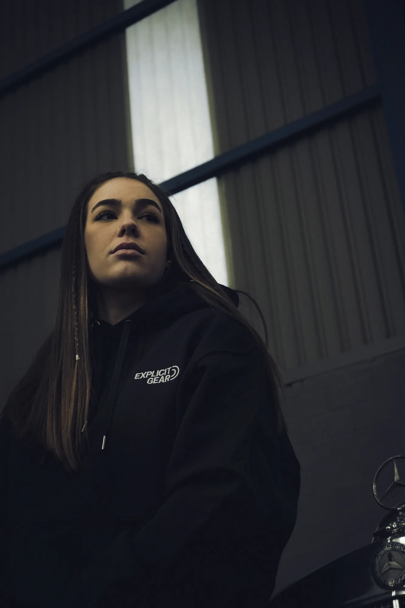 Chica con la sudadera negra de Explicit Gear junto a una ventana del garaje