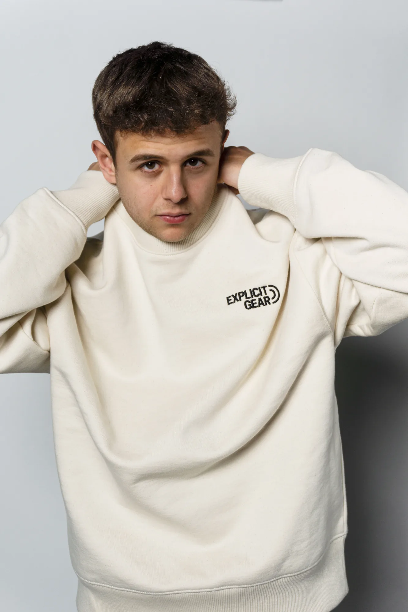 Chico con la sudadera crema de Explicit Gear y las manos en la nuca