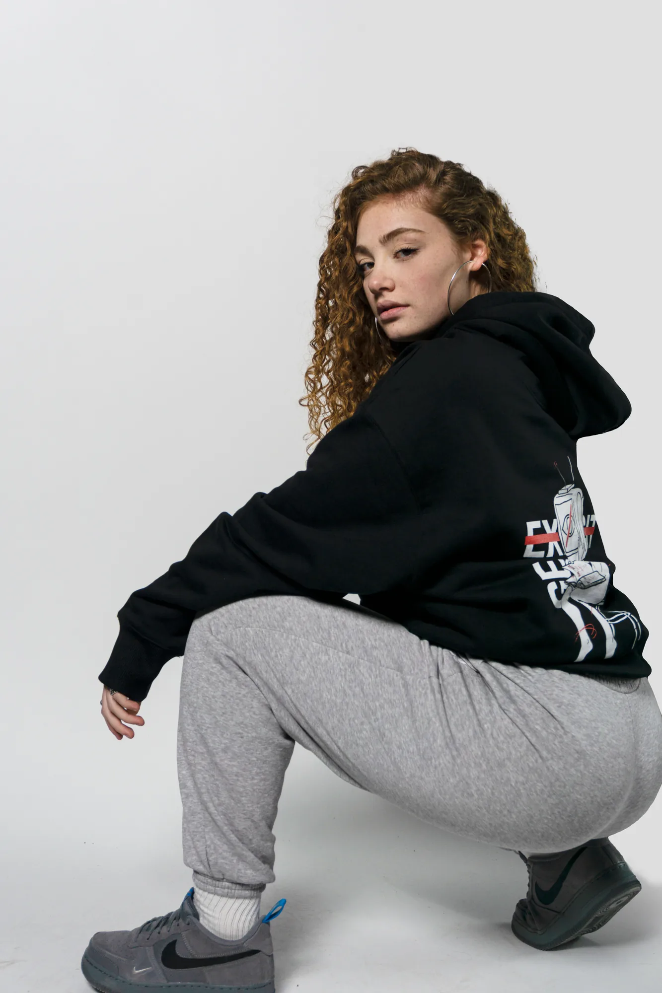 Chica agachada con la sudadera negra de Explicit Gear