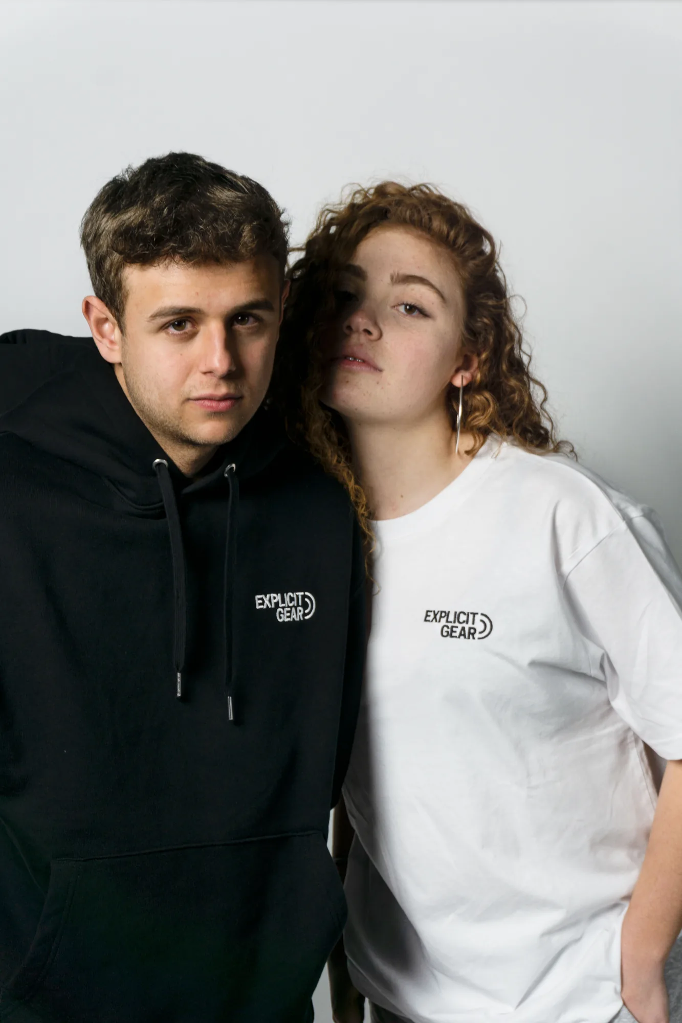 Pareja con sudadera negra y camiseta blanca, mirando a cámara