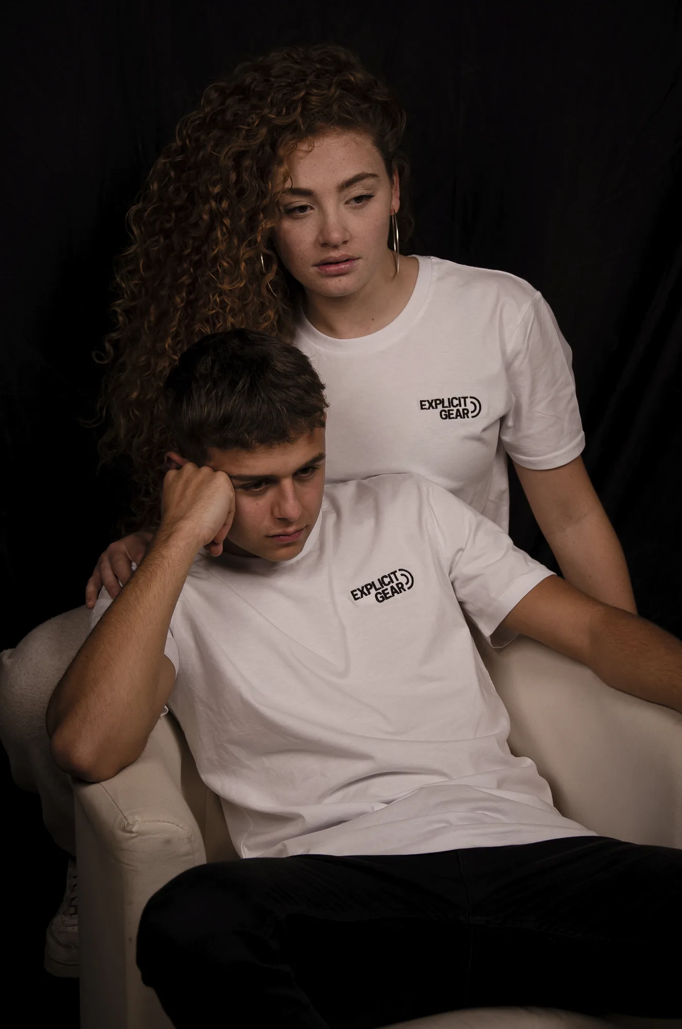Pareja con camisetas blancas de Explicit Gear en un sillón