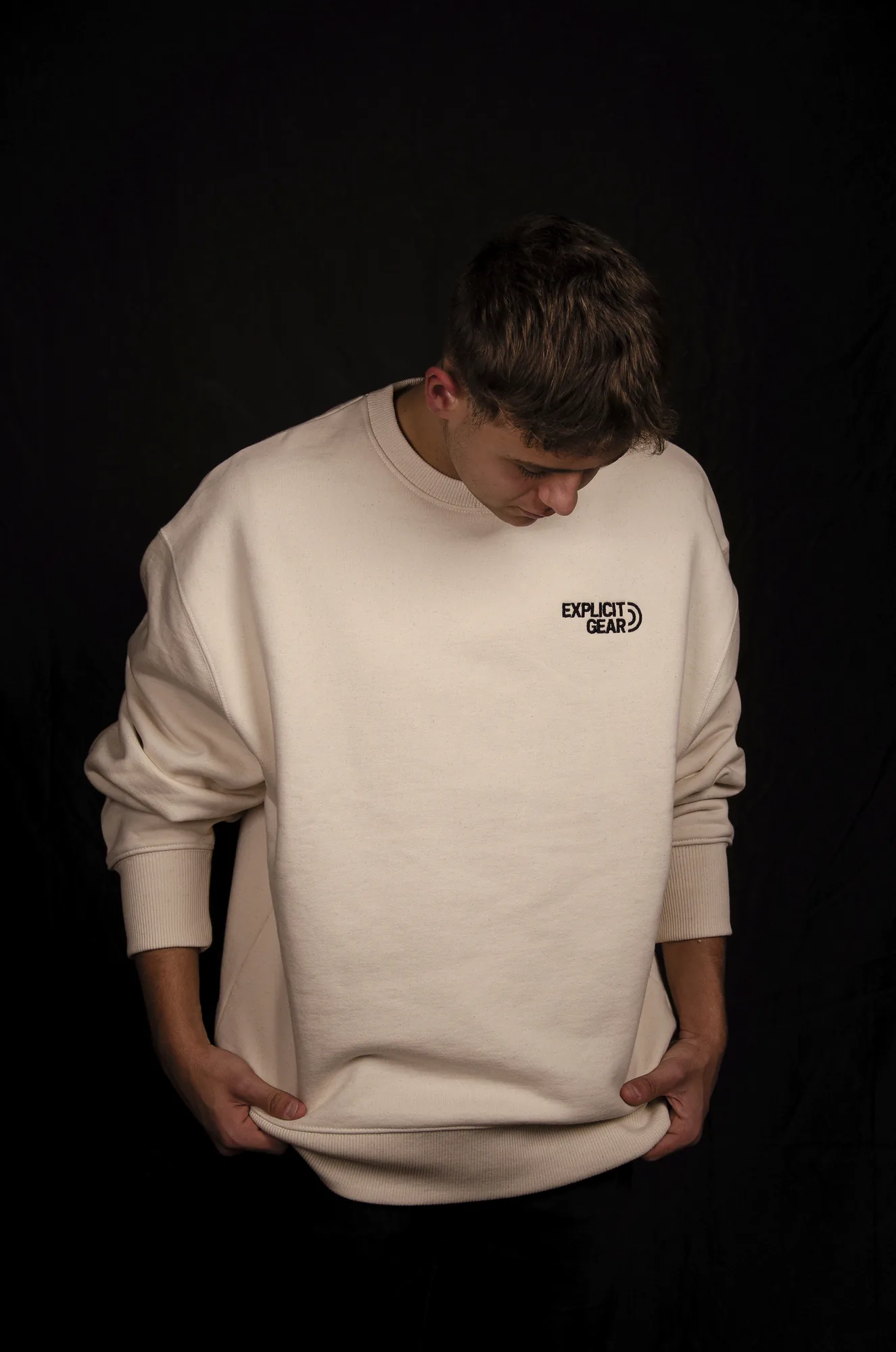 Chico con la sudadera crema de Explicit Gear mirando hacia abajo