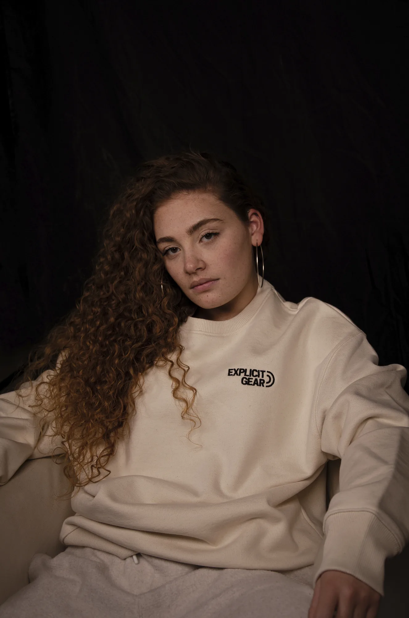 Chica con la sudadera crema de Explicit Gear sentada en un sillón