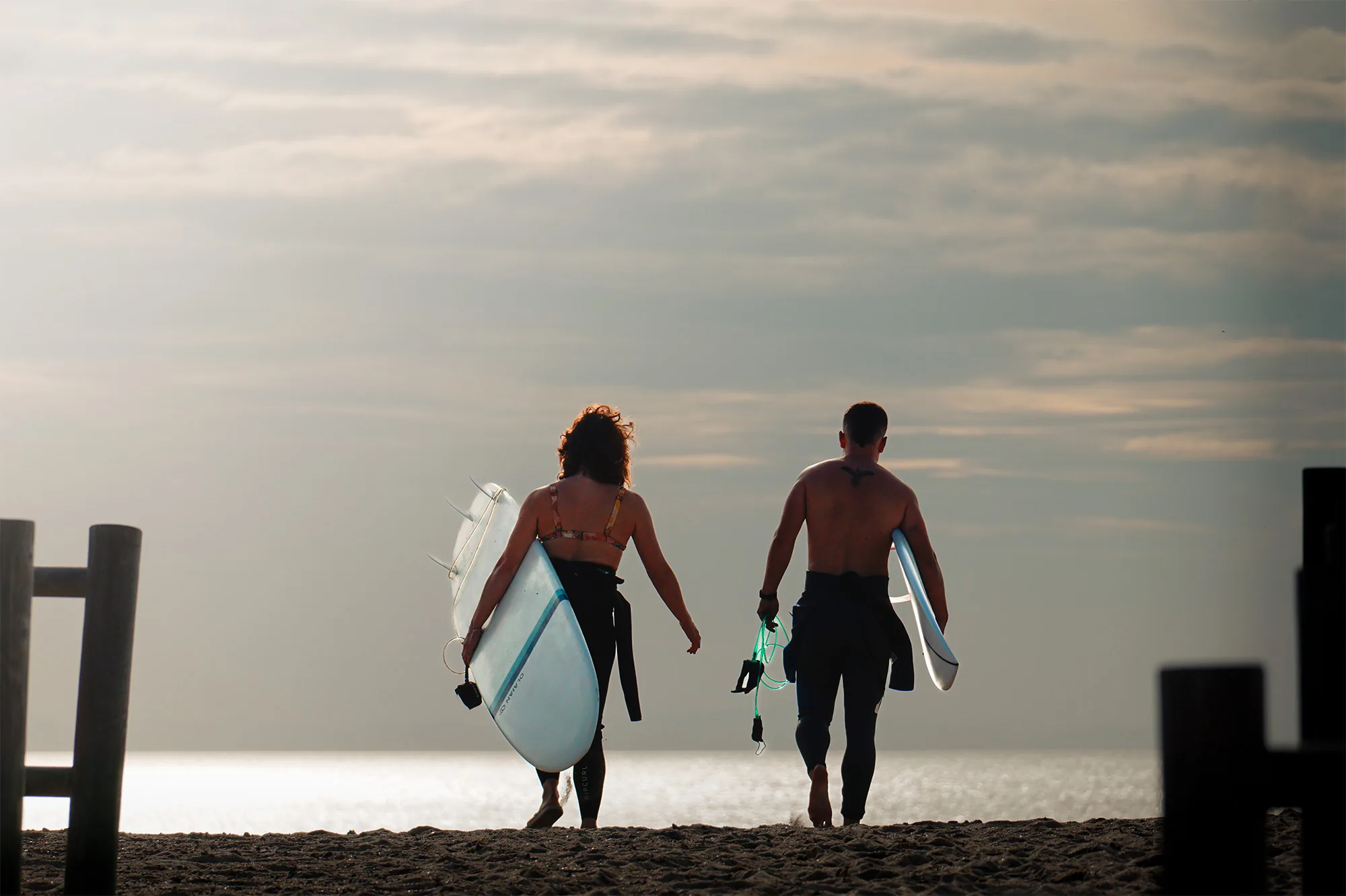 Dos surfistas caminando hacia el mar al atardecer