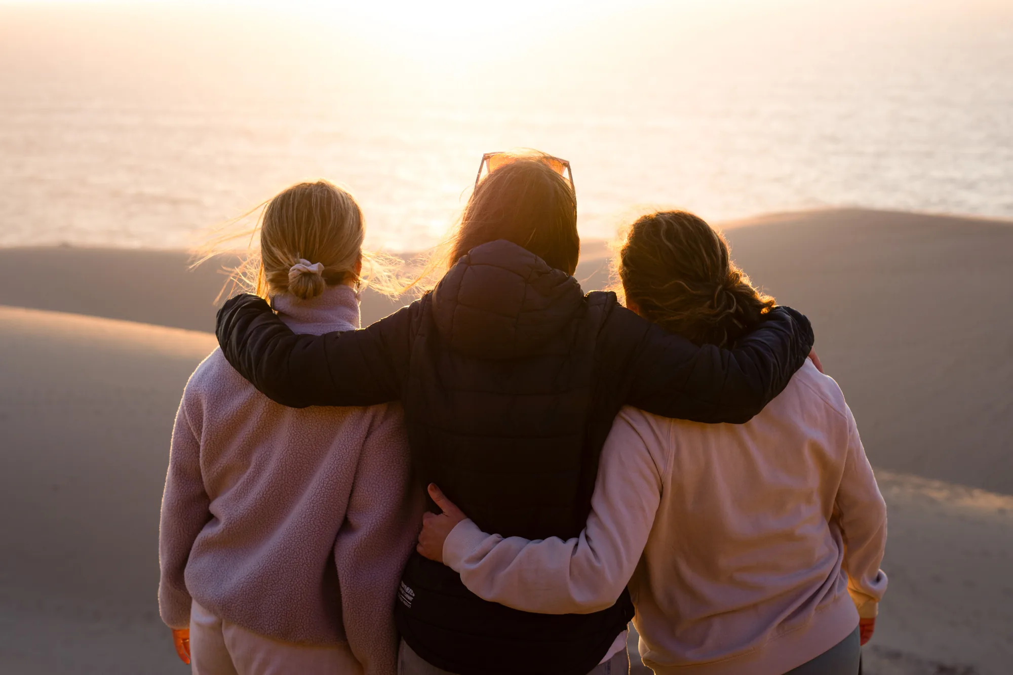 Tres amigas abrazadas mirando el atardecer en las dunas