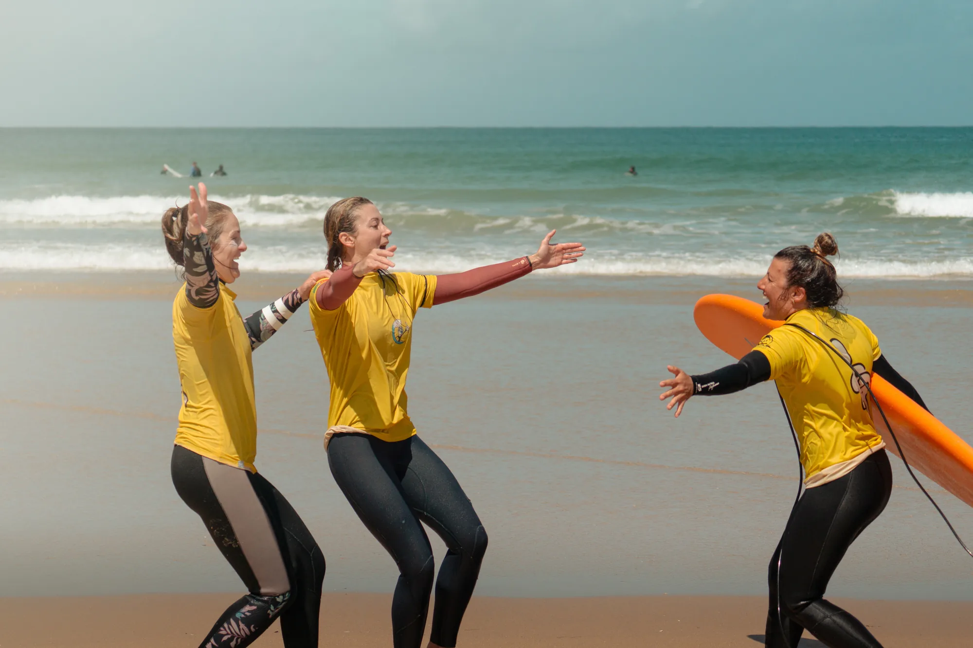 Tres surfistas con licra amarilla saltando en la orilla